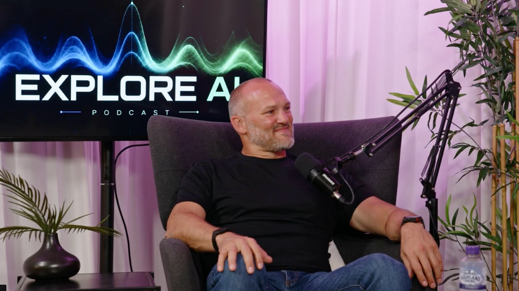 The Studio at River House: a guest seated in an armchair in front of a screen showing the Explore AI Podcast branding